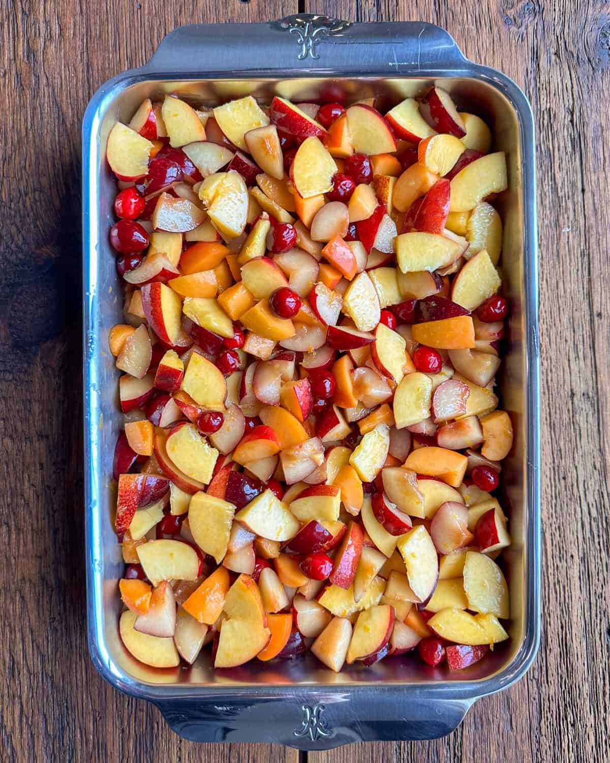 A baking dish with stone fruit, cranberries, sugar, honey, cornstarch, orange zest, and juice.