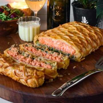 A sliced salmon en route with Leeks on a cutting board with wine and sauce.