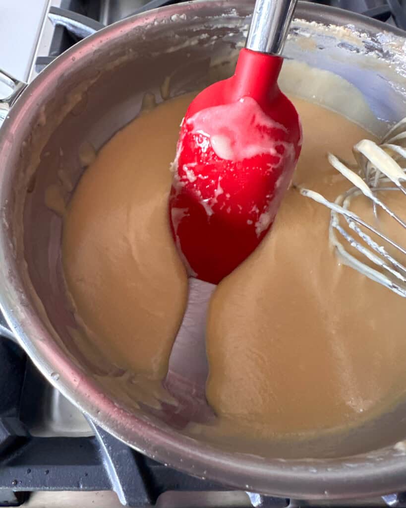 A sauce in a sauier with a spatula and whisk.