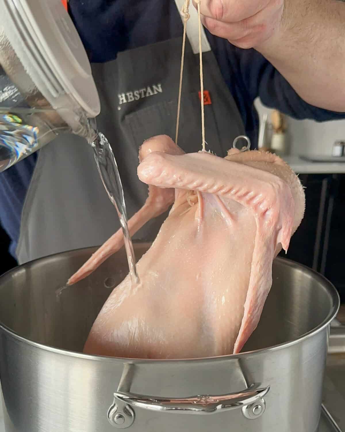 Use butcher's twine, placed under the wings to hold the duck above a large pot and carefully pour the boiling hot water over the duck to scald and tighten the skin up.