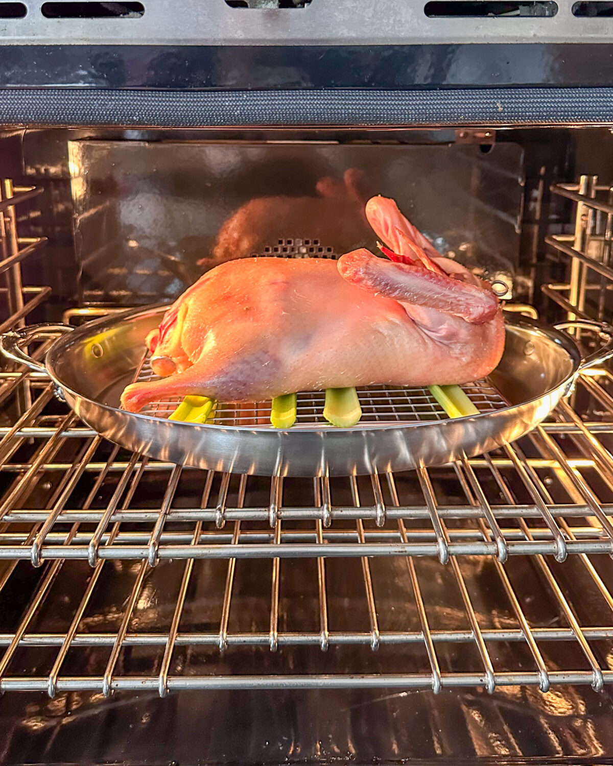 A Peking style duck, breast-side down in a roaster in the oven.
