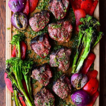 A board with grilled lamb chops with a poblano board sauce and grilled vegetables.