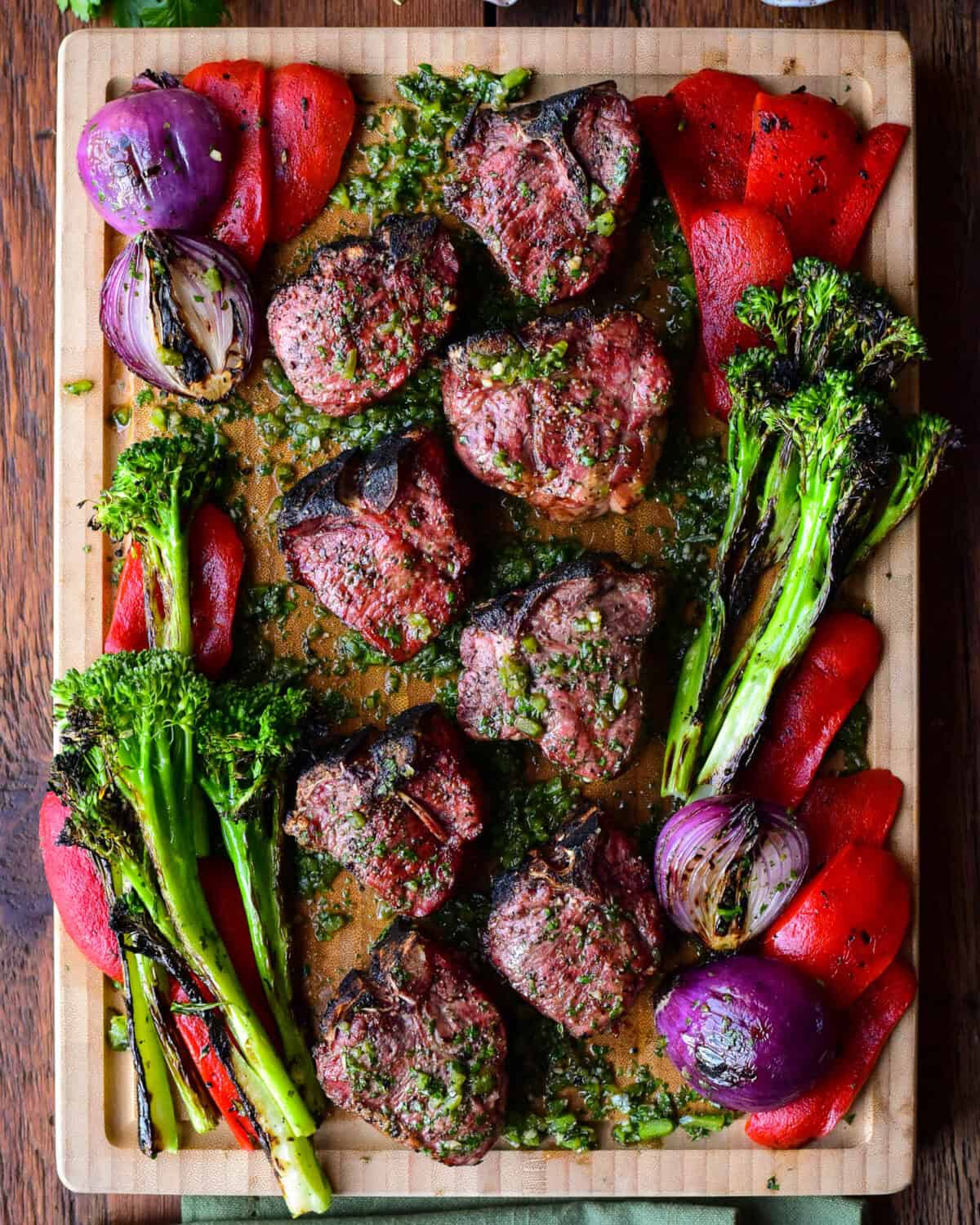 A board with grilled lamb chops with a poblano board sauce and grilled vegetables.