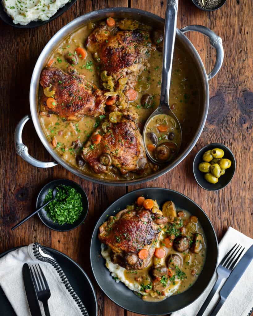 A pan of golden brown turkey thighs braised in a mushroom wine sauce served with mashed potatoes, and chopped parsley.