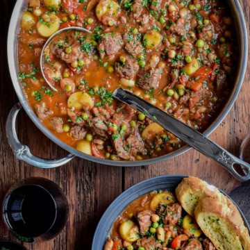 A large pot of Spanish Lamb Stew with a ladle and a bowl served with crusty bread.
