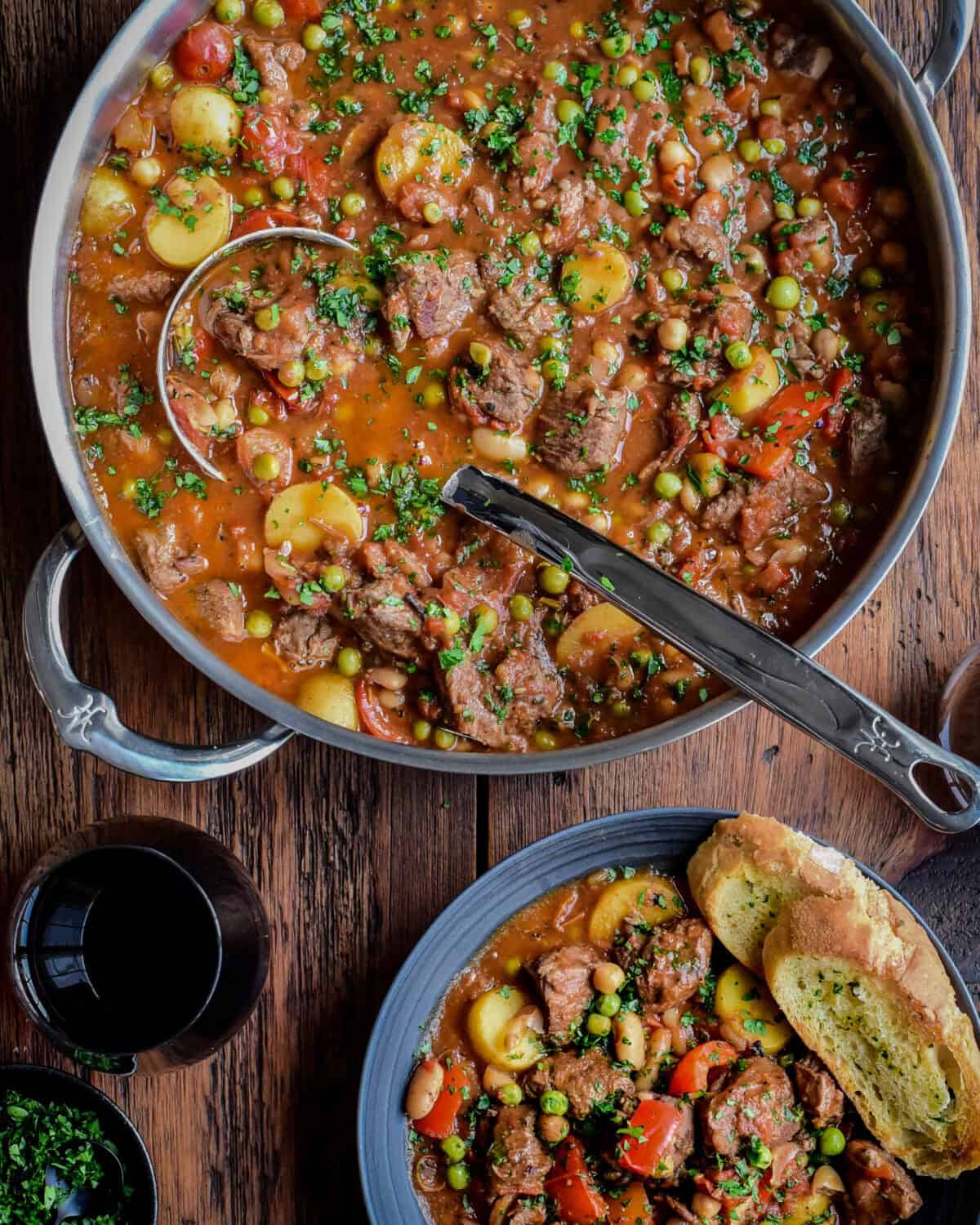 A large pot of Spanish Lamb Stew with a ladle and a bowl served with crusty bread.