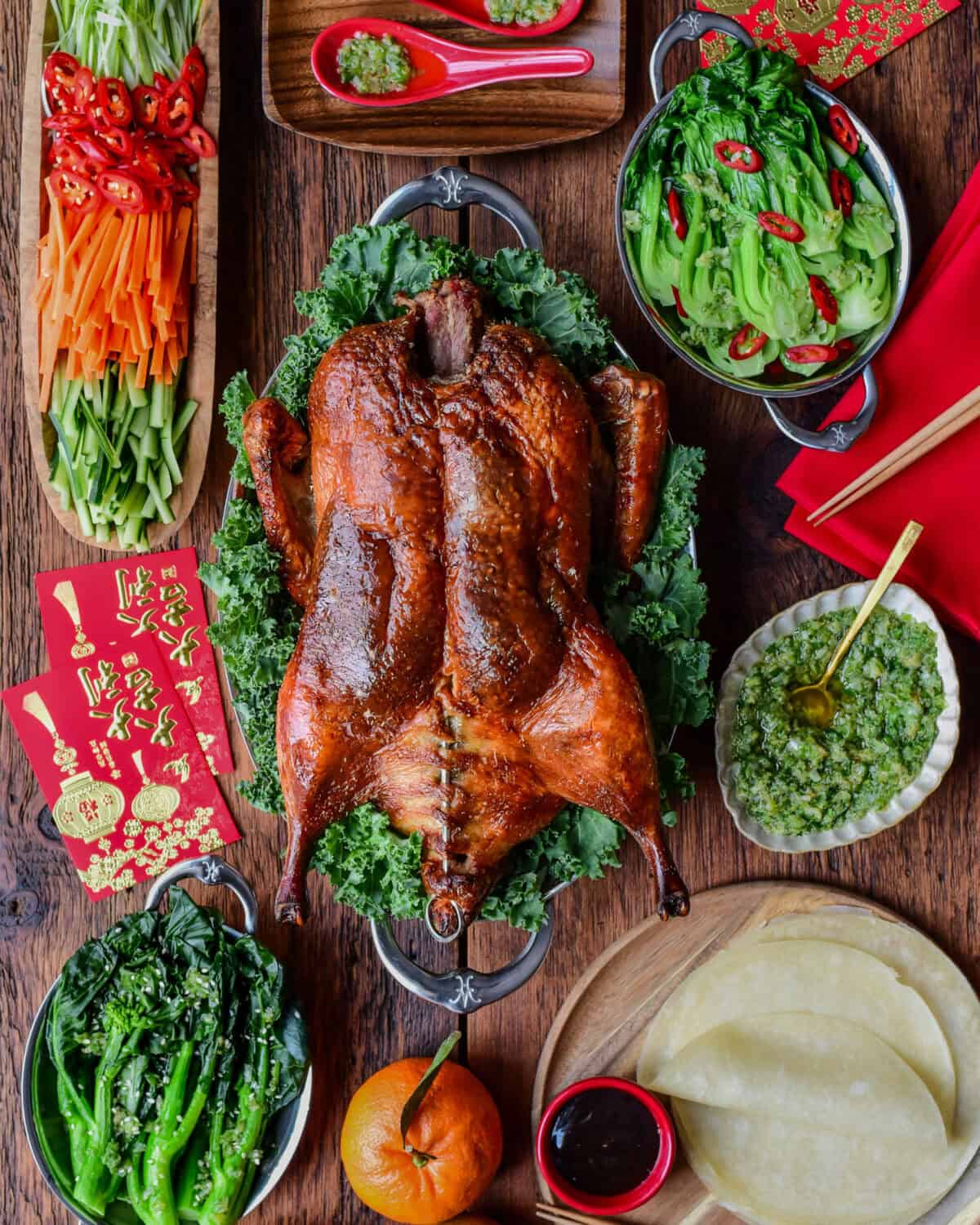 A whole crispy Peking duck served with hoisin sauce, ginger scallion sauce, pancakes, green onions, carrots, cucumber, and chilies.