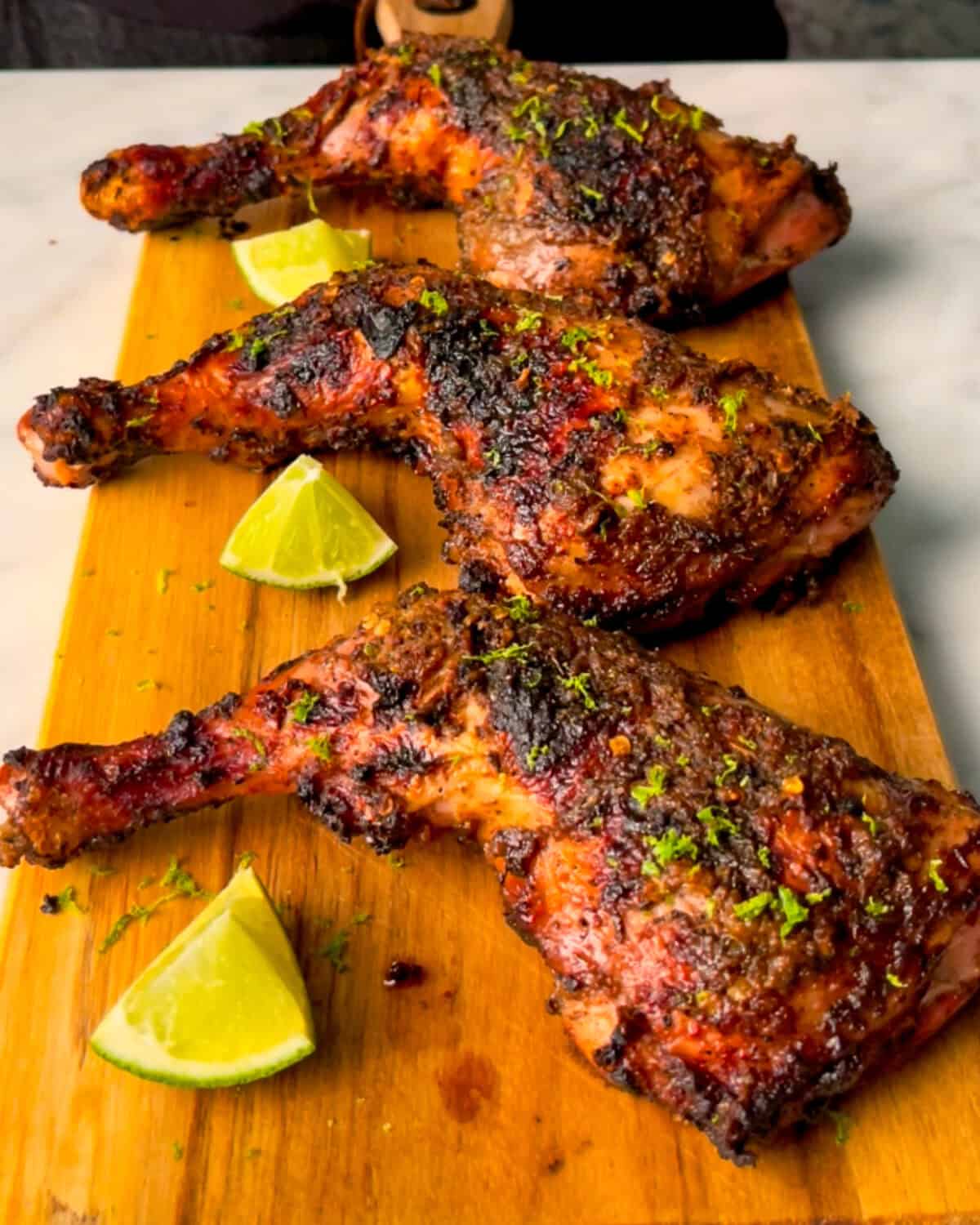 Three Jerk Chicken Leg Quarters served with lime wedges and zest.