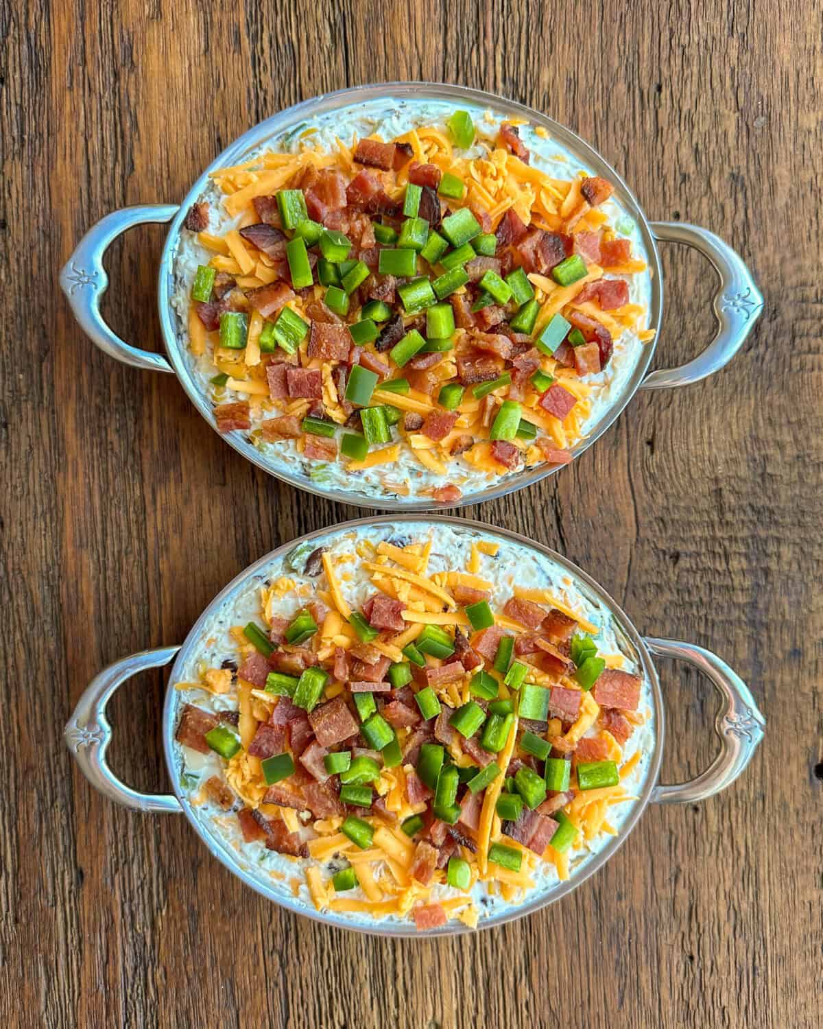 Two au gratin dishes with a cheese dip mixture and toppings.