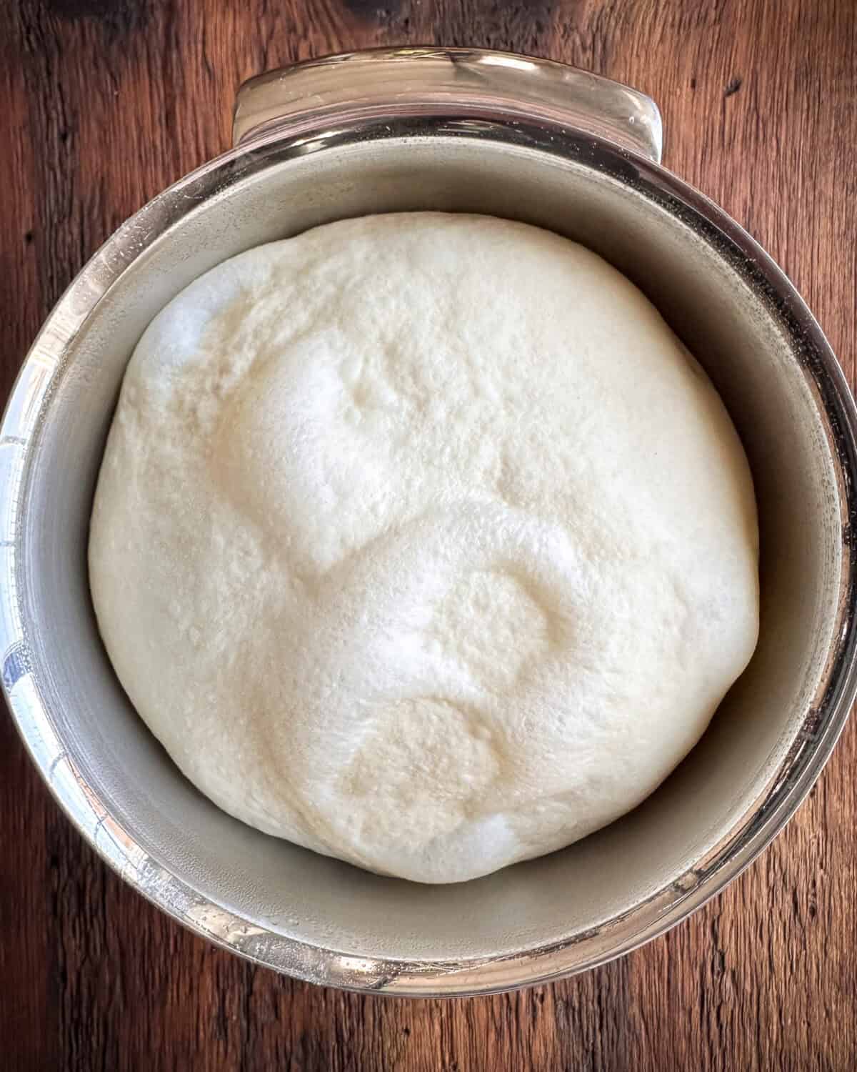 A pizza dough ball in a mixing bowl that has doubled in size.