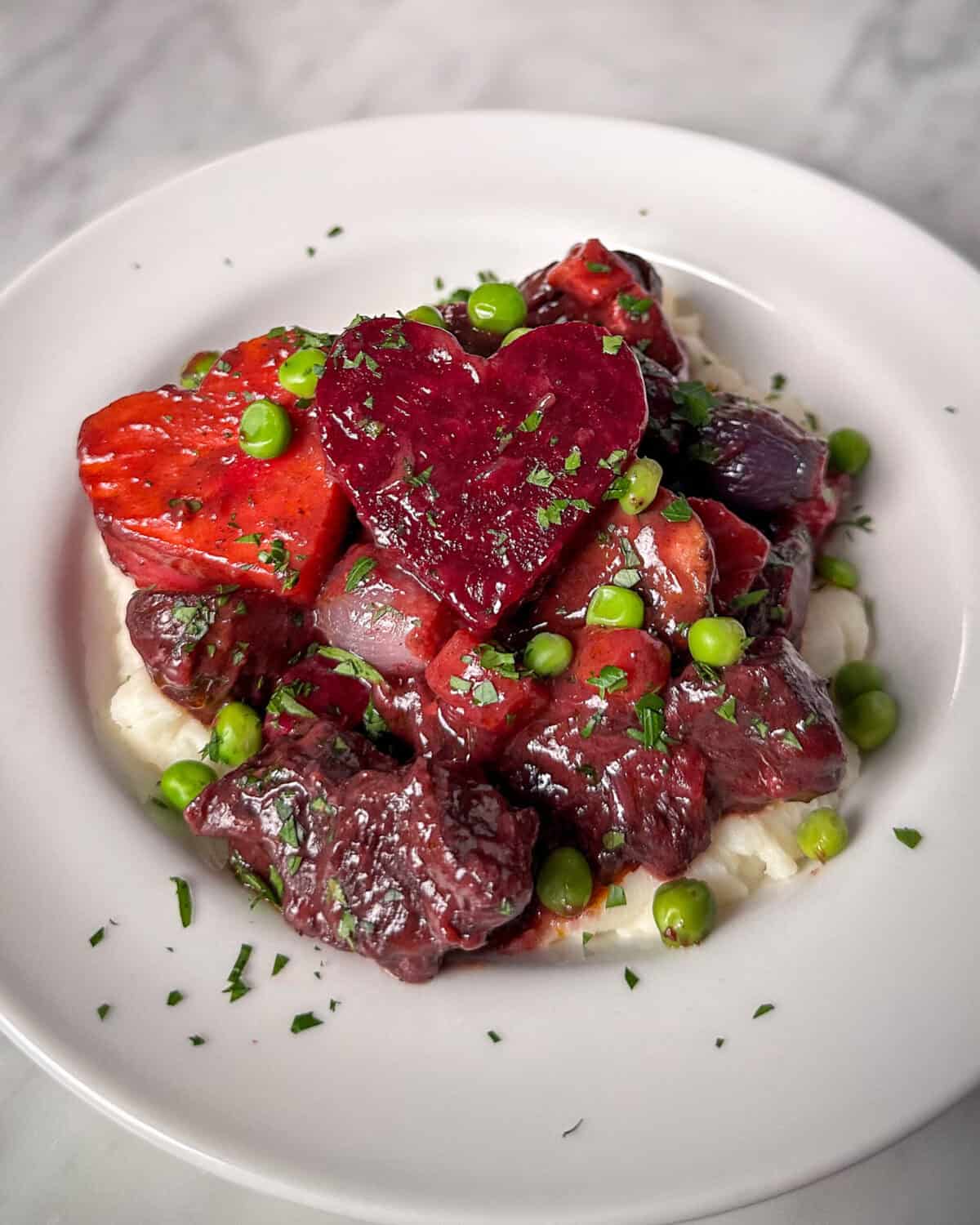A bowl of beef bourguignon with mashed potatoes and beet hearts.