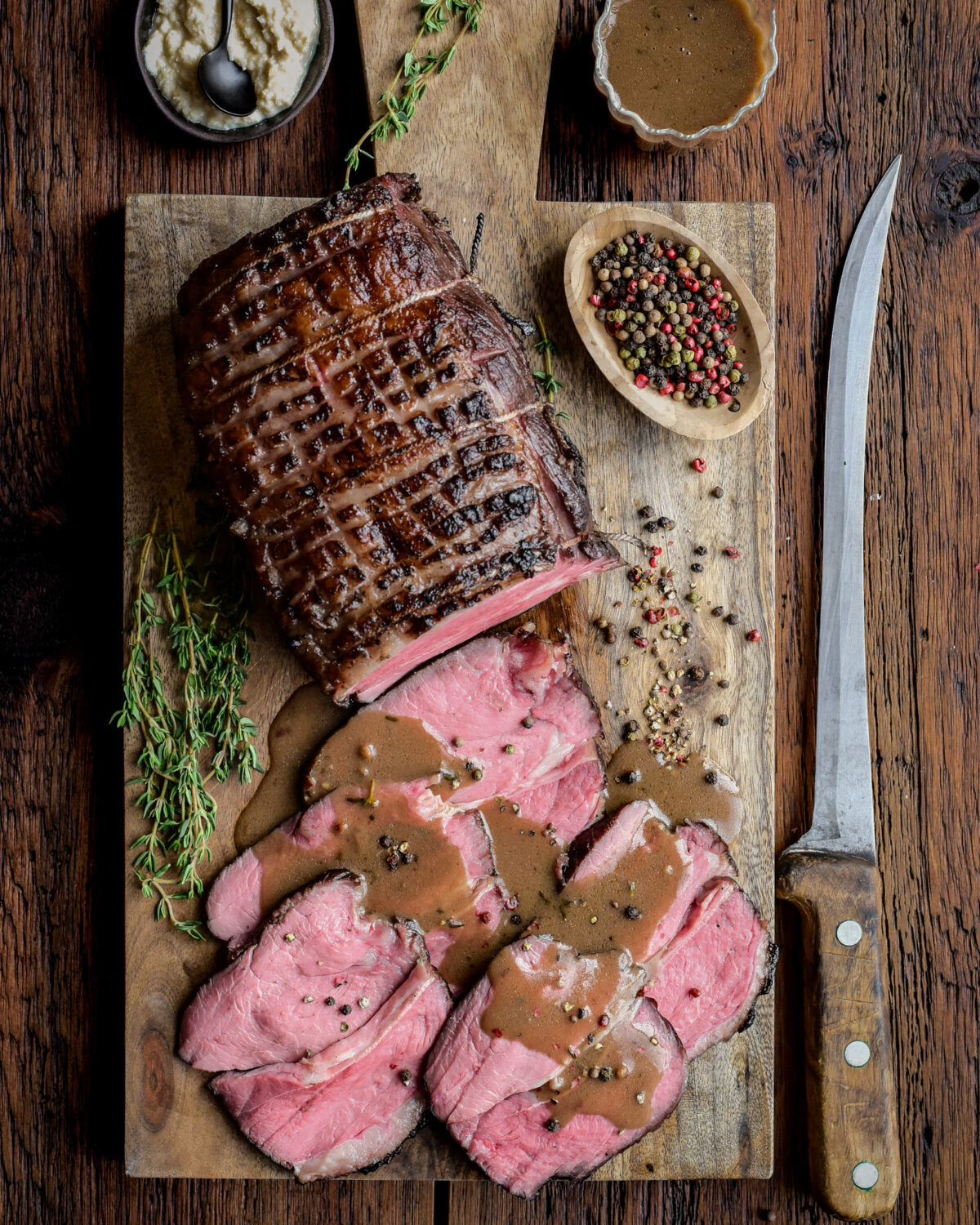 A sous vide roast beef with half of it sliced with some Marsala pepper sauce poured over top.