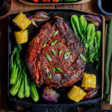 An Asian-Glazed Prime Rib Roast on an Ooni Grizzler Plate and served with a vegetable medley of bok choy, corn, carrots, red onions and red peppers.