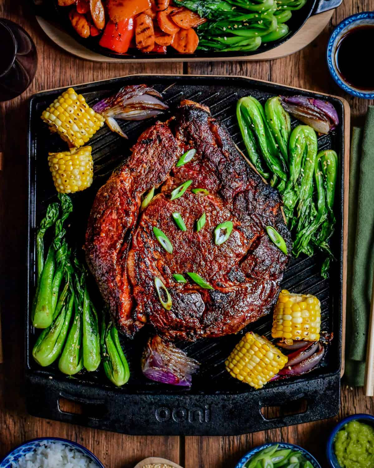 An Asian-Glazed Prime Rib Roast on an Ooni Grizzler Plate and served with a vegetable medley of bok choy, corn, carrots, red onions and red peppers.