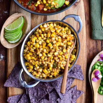 A bowl of Cajun corn served with tortilla chips, limes and chili.