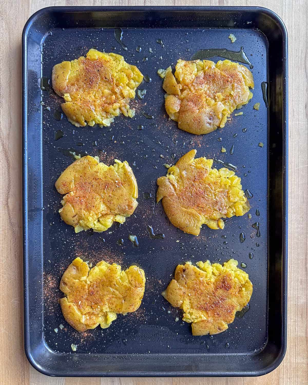 A sheet pan of eight smashed potatoes with seasoning.