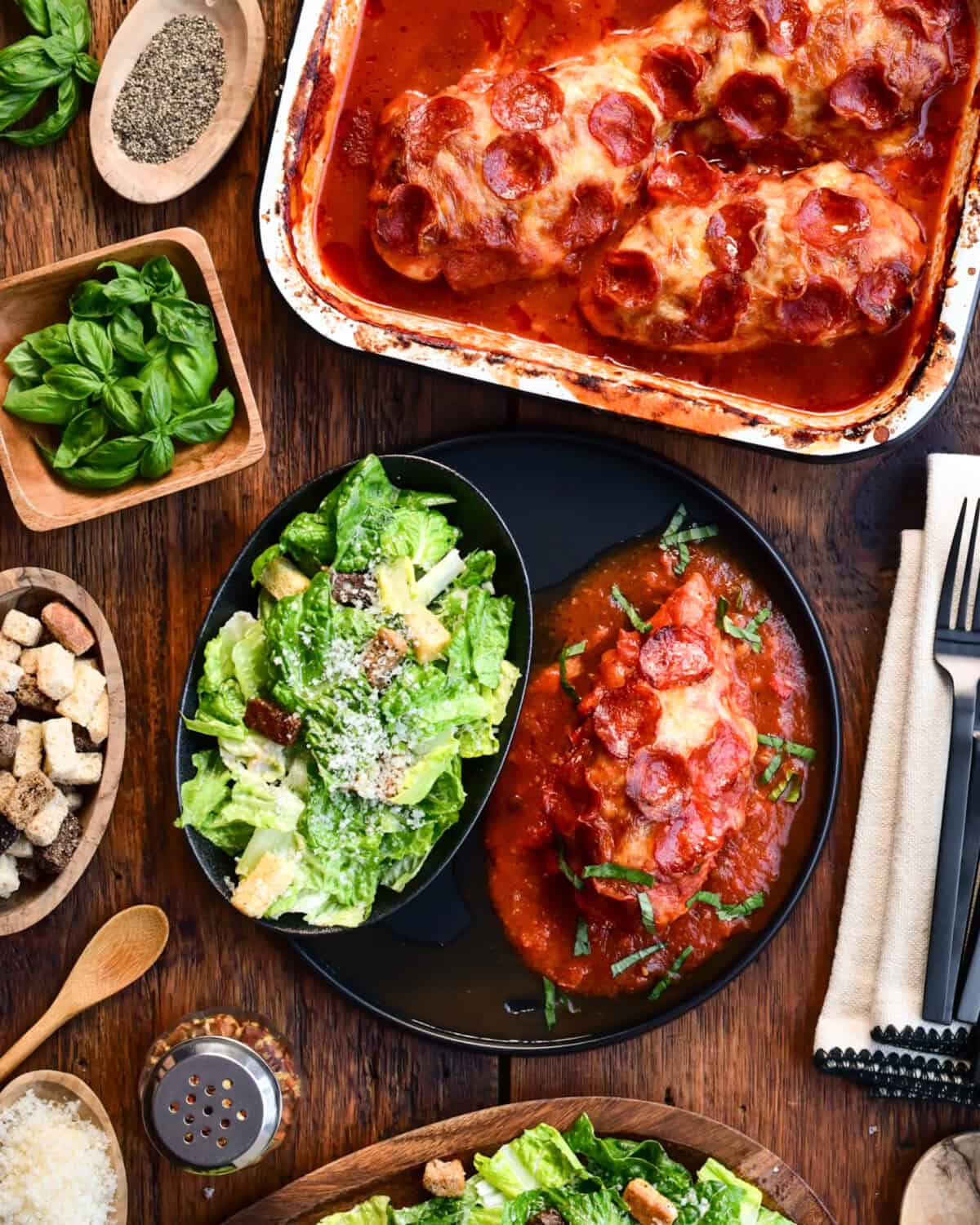 A baking pan with Chicken Pizzaiola with Pepperoni. As well as one plated with a side of Caesar salad.