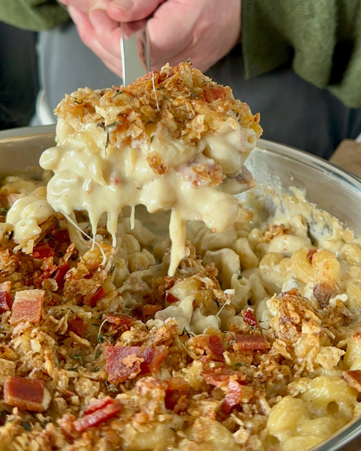 Lifting a scoop of three cheese mac and cheese out from a pan.
