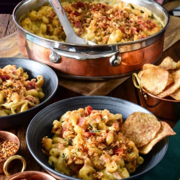A copper pot and two bowls of Guinness Mac and Cheese with Irish Whiskey Onions. Served with chips and Guinness.