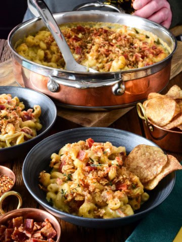 A copper pot and two bowls of Guinness Mac and Cheese with Irish Whiskey Onions. Served with chips and Guinness.