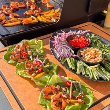 Griddle shrimp wraps on a griddle side table with toppings and extra shrimp and mango keeping warm on the griddle.