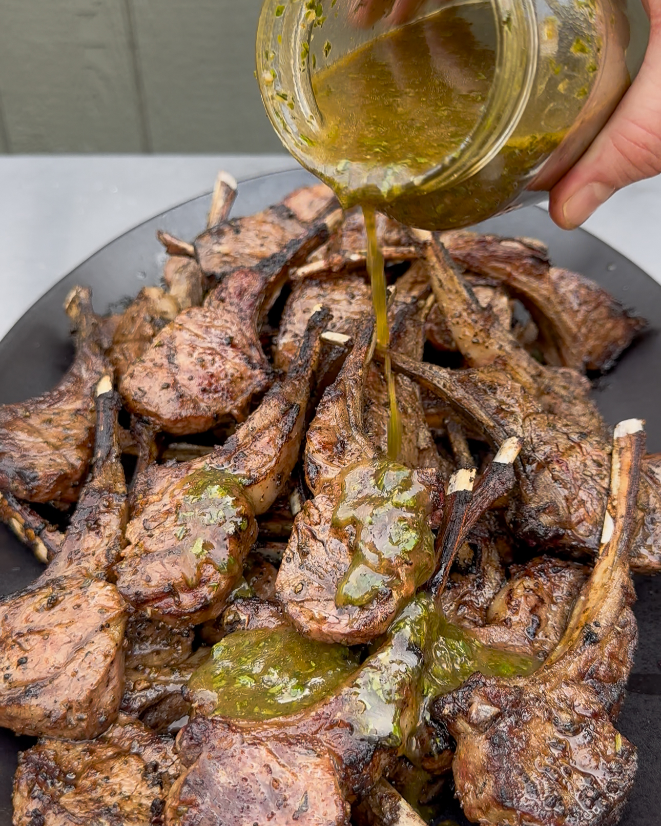 An herb sauce for lamb is being poured over a platter of lamb.