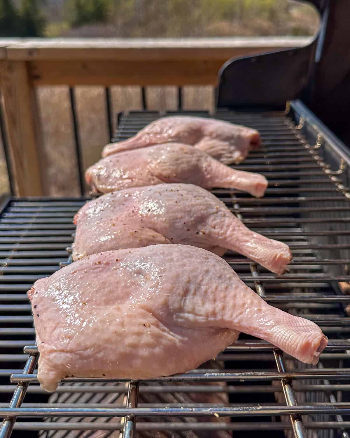 Four duck legs on a pellet smoker, skin side up.