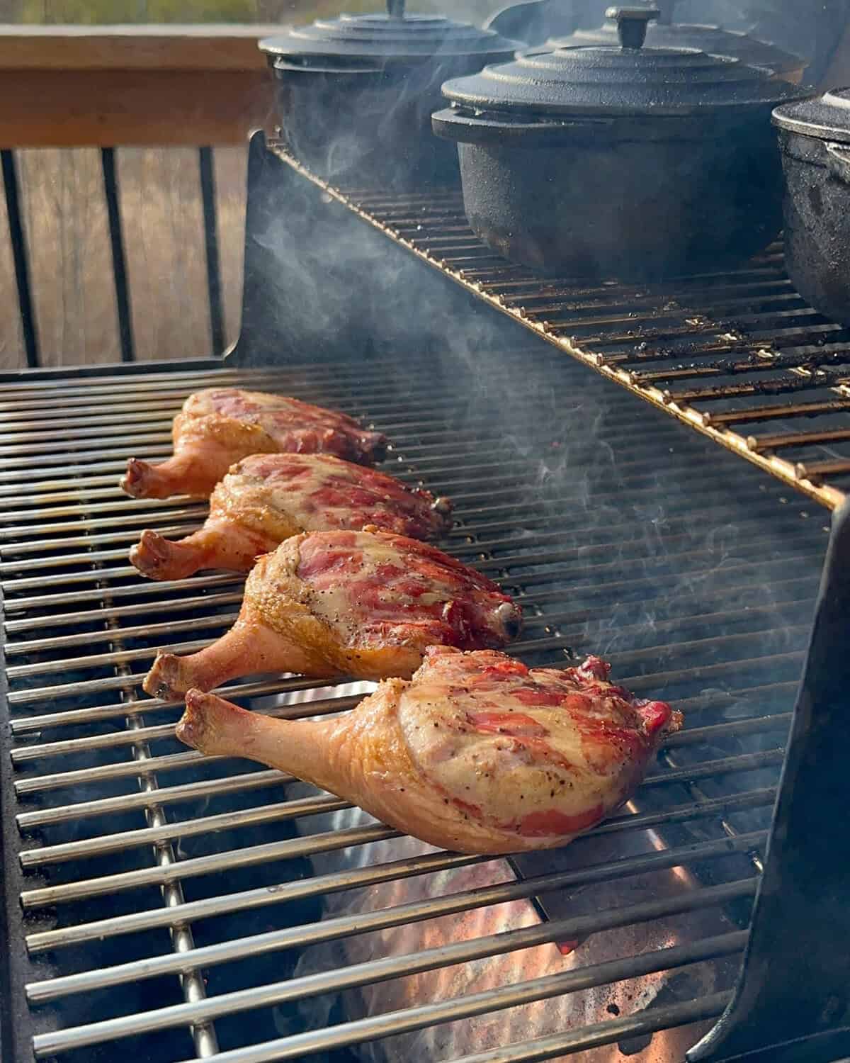 Four smoked duck legs on the bottom rack of a smoker are getting seared.