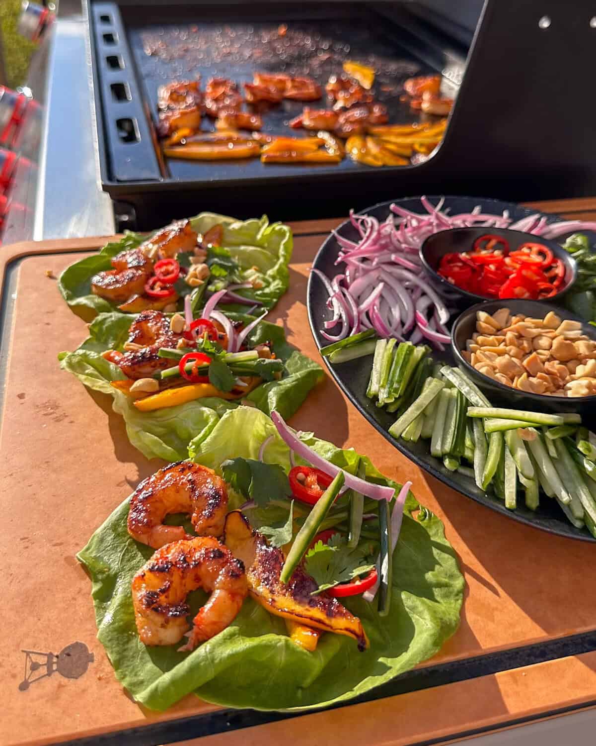 Three assembled Griddled Shrimp & Charred Lettuce Wraps on the side table of a griddle.