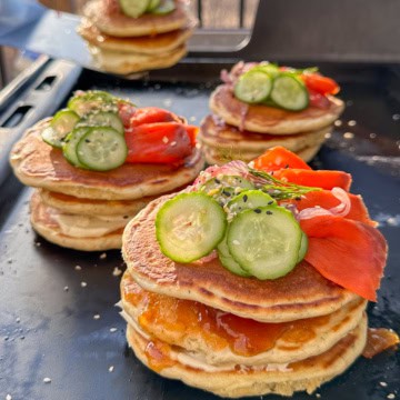 Four stacks of Lemon Dill Pancakes with Smoked Salmon and Mango Chutney on an outdoor griddle.