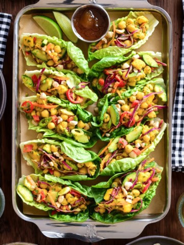 Colorful vegan mango chickpea lettuce wraps with red onion, avocado, and a side of dipping sauce, perfect for a picnic or light meal.