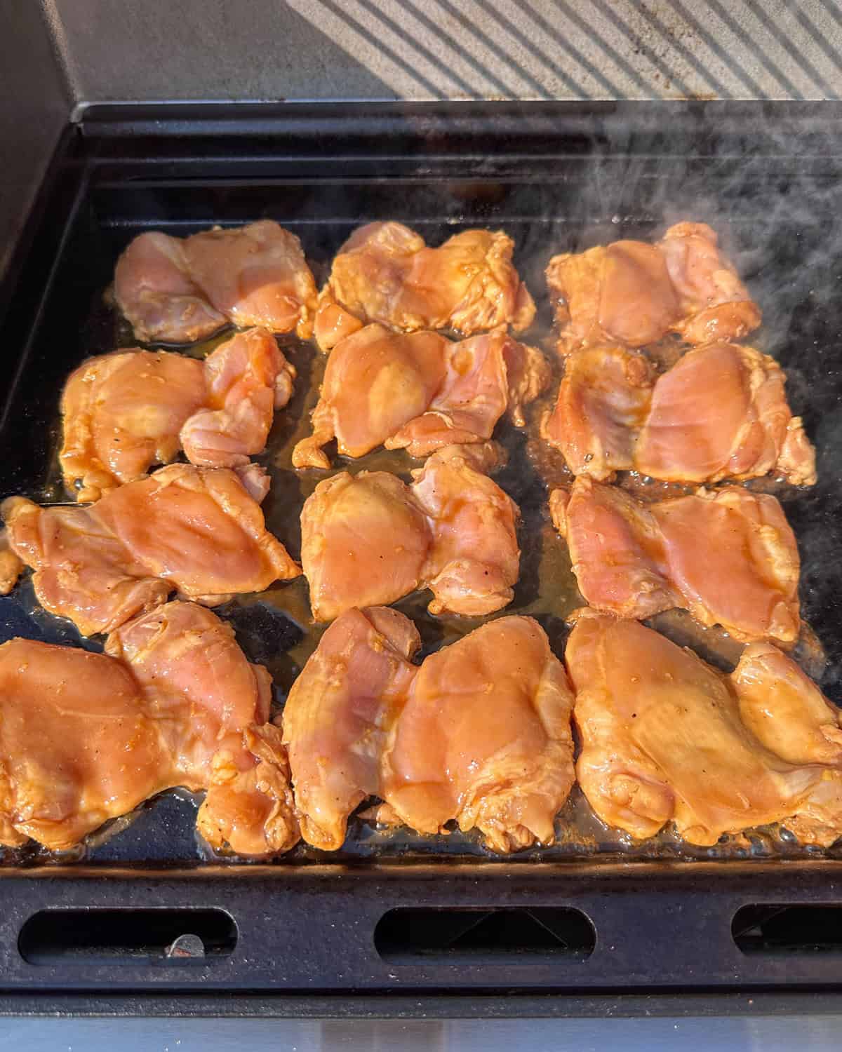 Twelve teriyaki-marinated chicken thighs on a griddle.