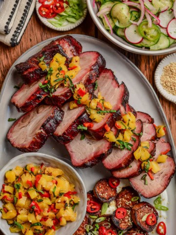 Slices of smoked char siu pork with a pineapple relish overtop and served with a cucumber salad and sweet potatoes.
