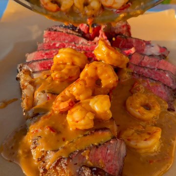 A grilled steak and shrimp image with the shrimp sauce getting poured over the steak.