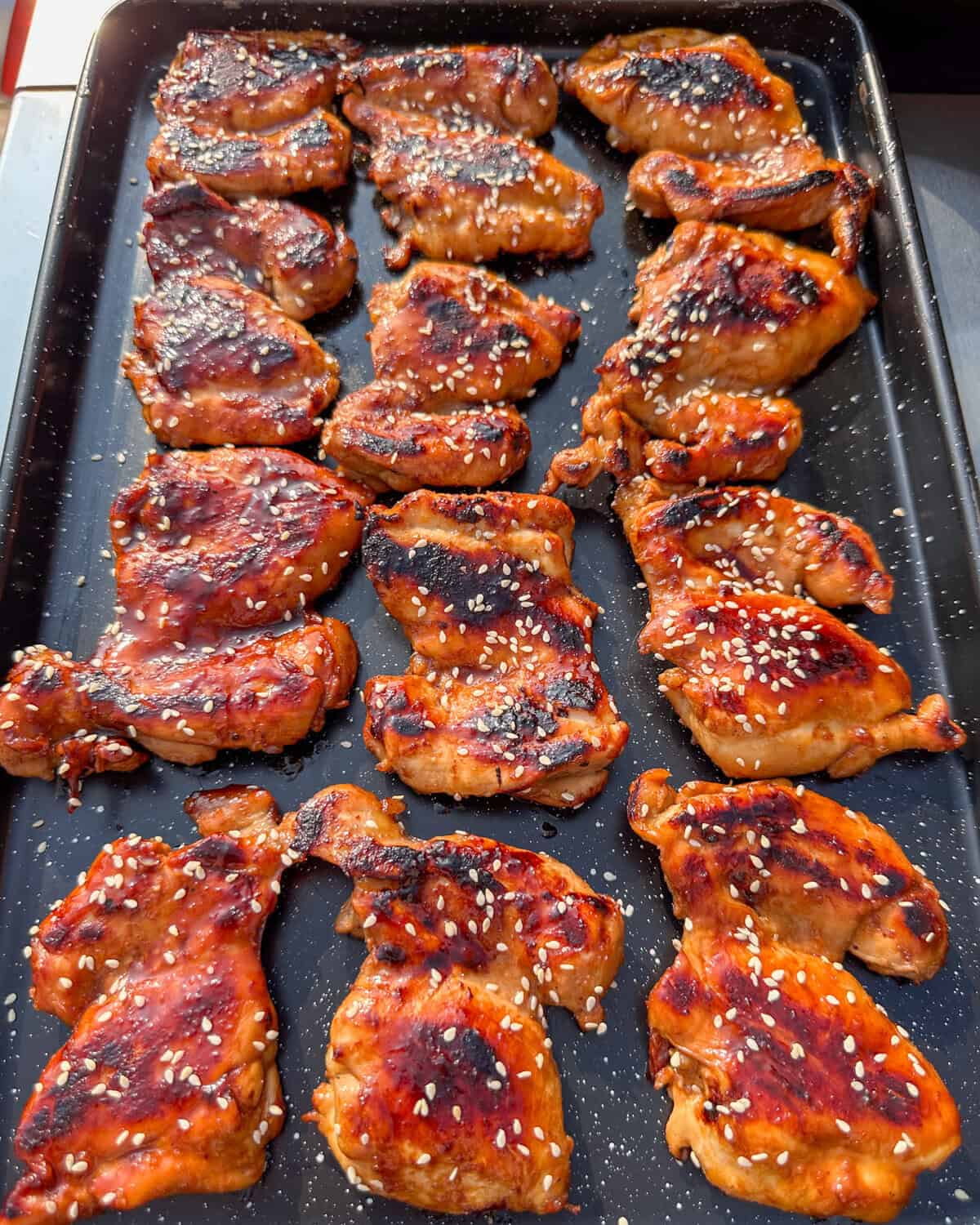 Teriyaki chicken on a sheet pan finished with sesame seeds.