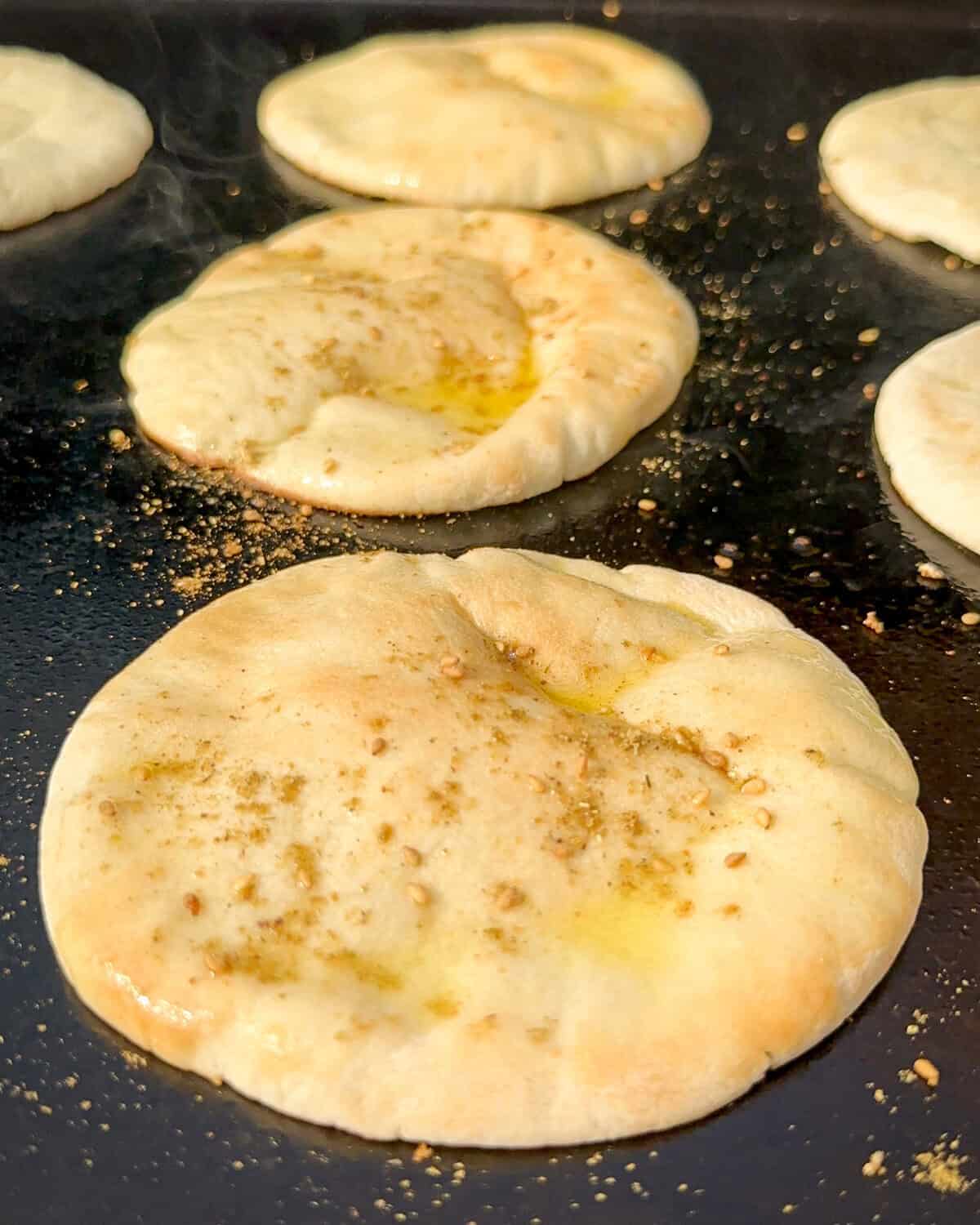 Mini pitas halves on the grill, brushed with olive oil and sprinkled with za'atar.