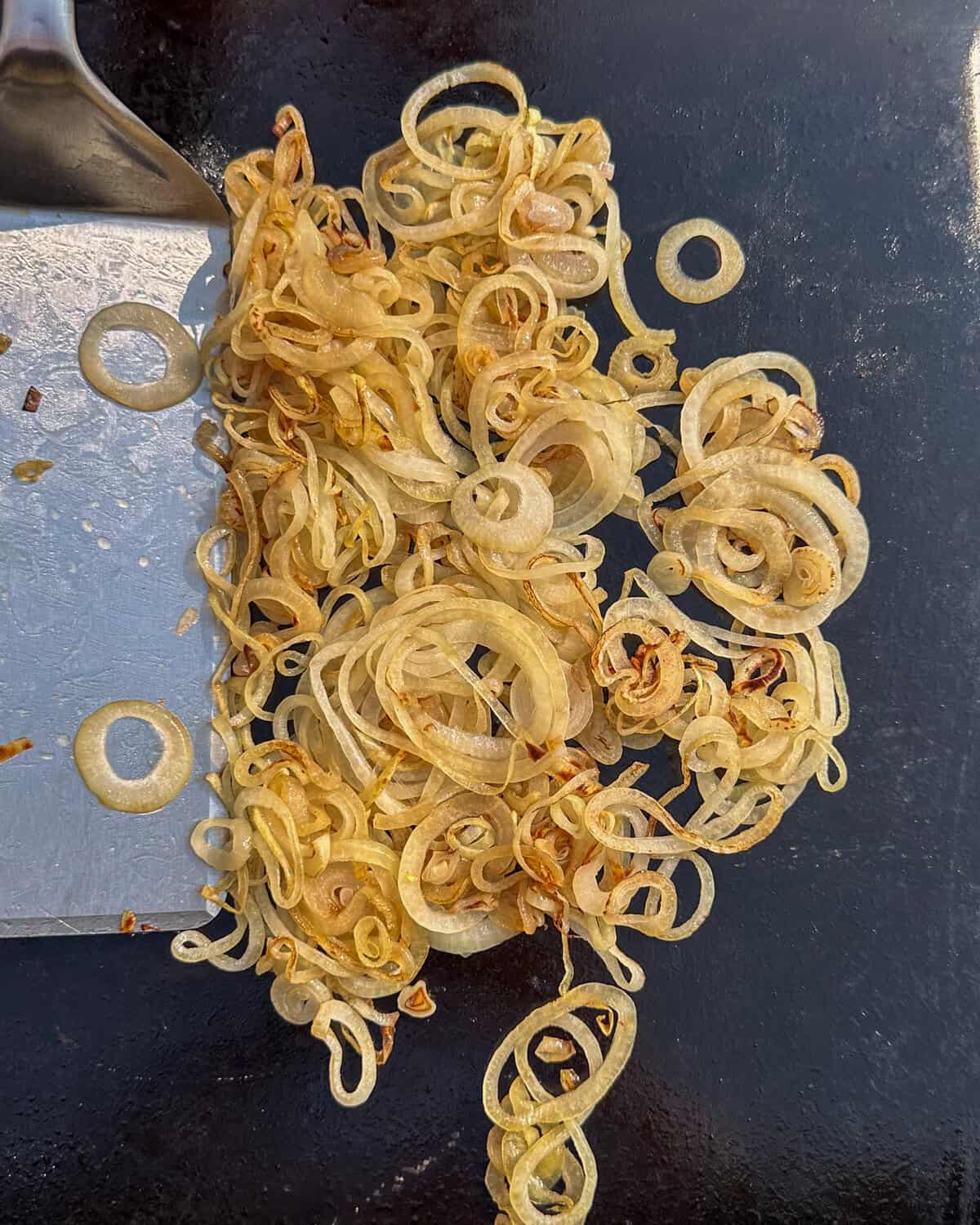 Golden griddled onions on a griddle with a lifter.