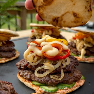 A double patty shawarma spiced lamb smash slider topped with onions, peppers and toum. The lid is being placed on the burger.