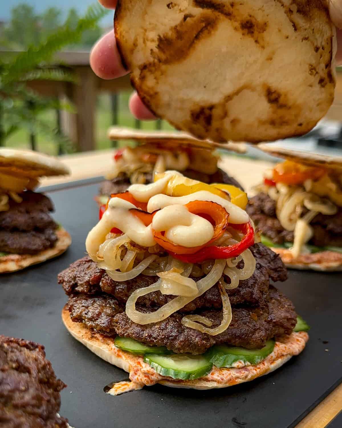 A double patty shawarma spiced lamb smash slider topped with onions, peppers and toum. The lid is being placed on the burger.