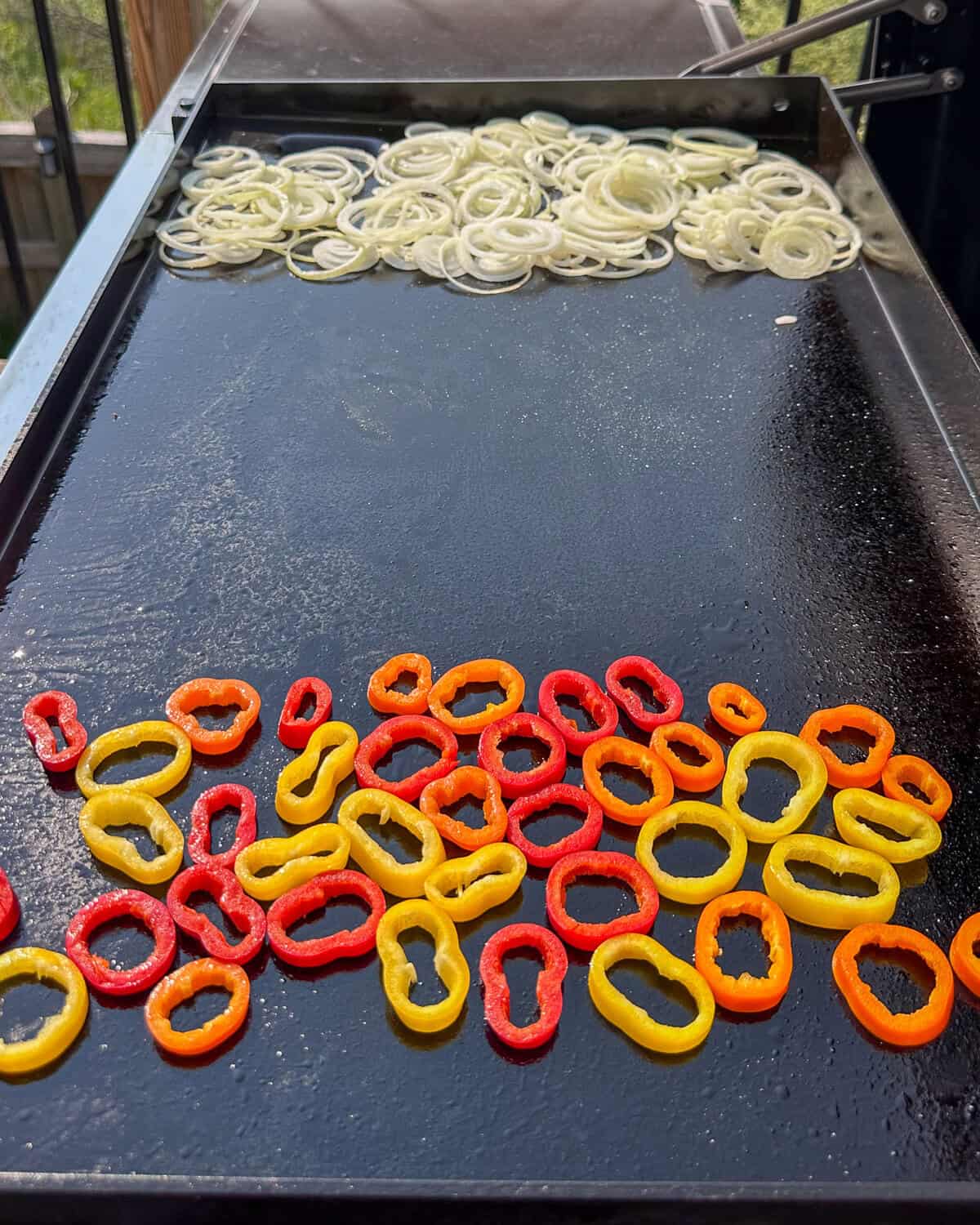 Griddled onions and peppers on a grill for lamb smash sliders.