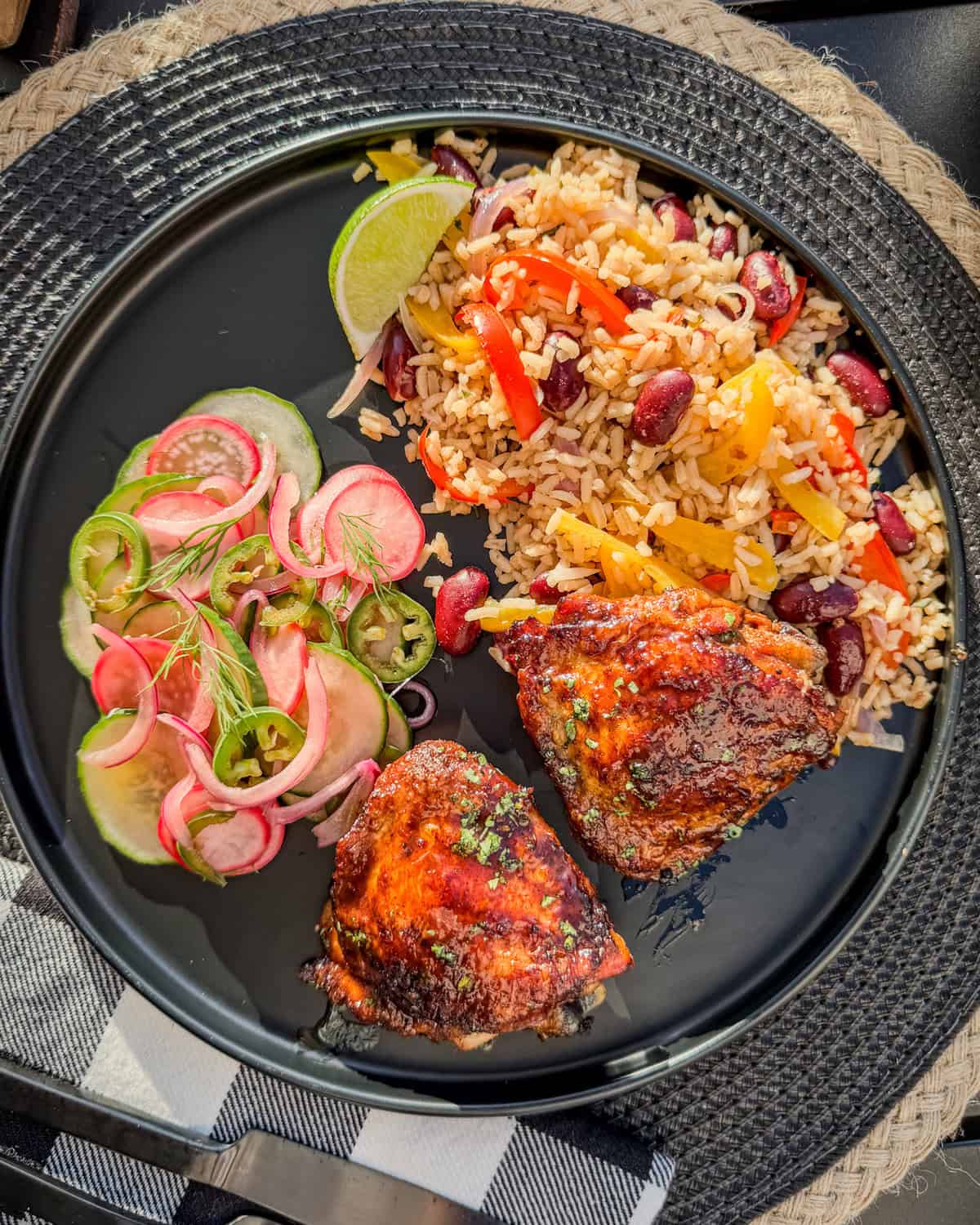 Sticky Rum Glazed Chicken Thighs, plated with Caribbean rice and beans, and a cucumber and radish salad.