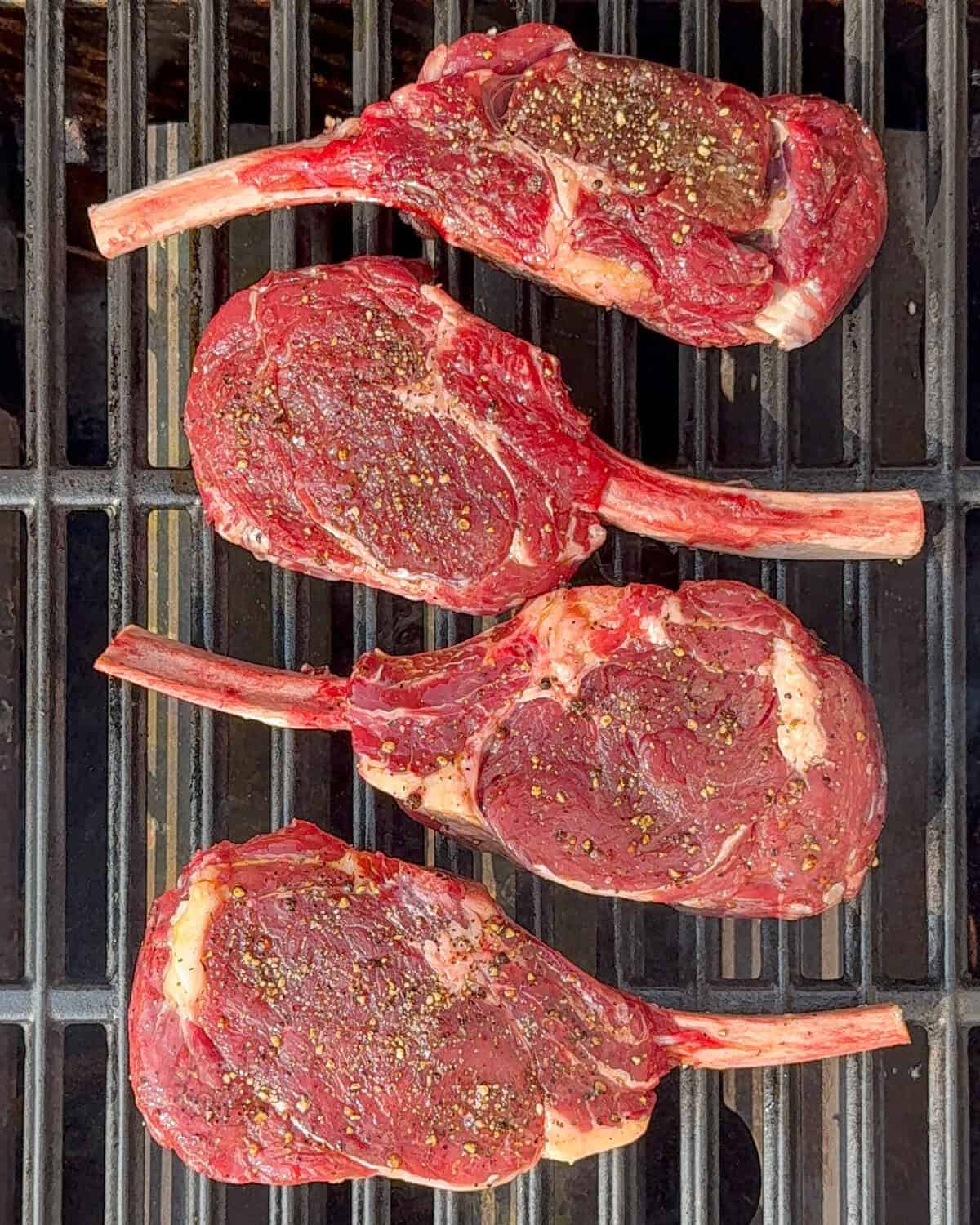 Four veal chops on a grill.