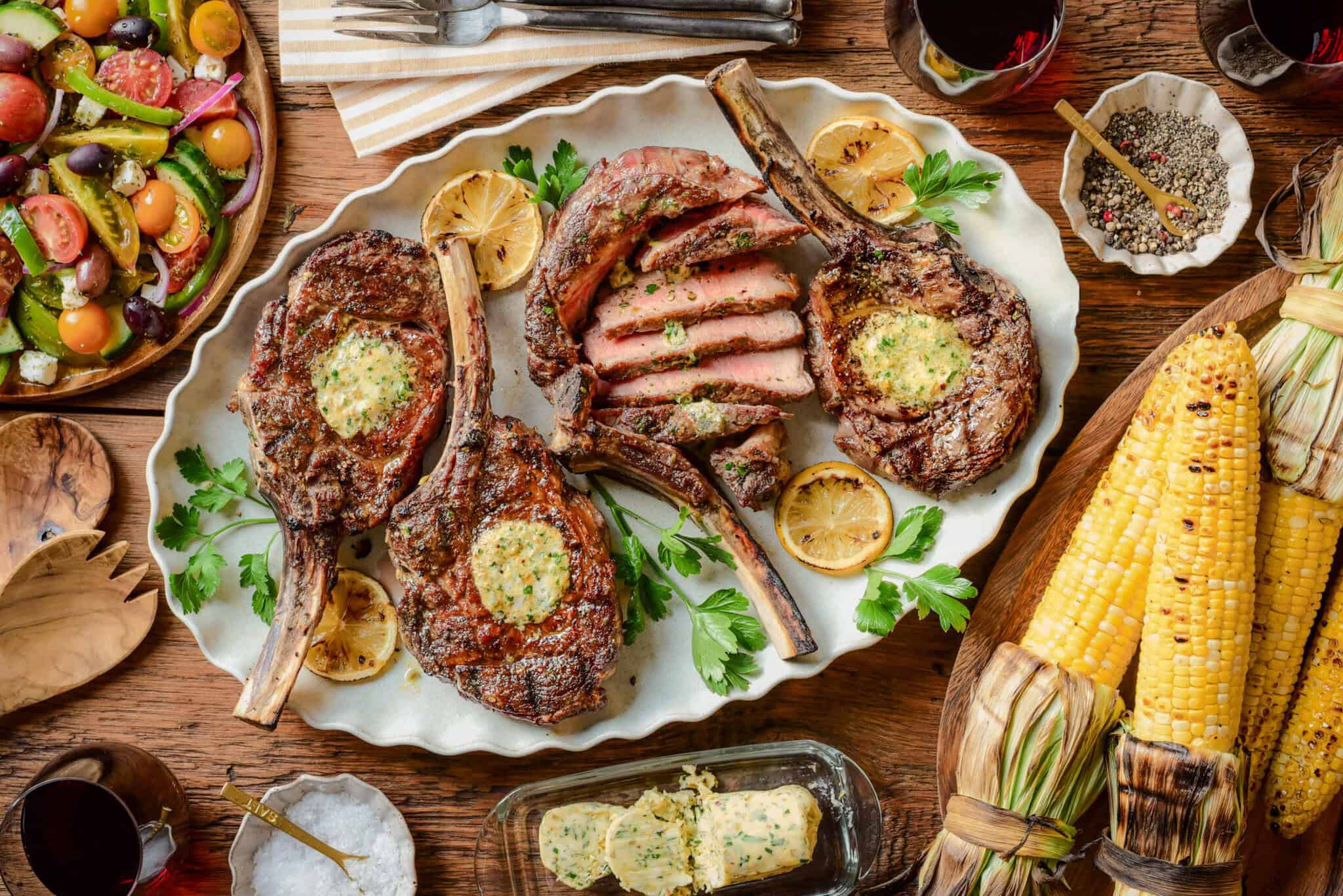Four grilled veal chops served with a village salad and grilled corn.