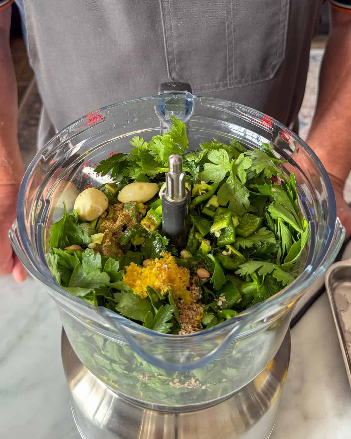 In a food processor, blend the zhoug ingredients: cilantro, parsley, garlic, chilies, cumin, cardamom, cloves, lemon zest and juice, olive oil, and salt.