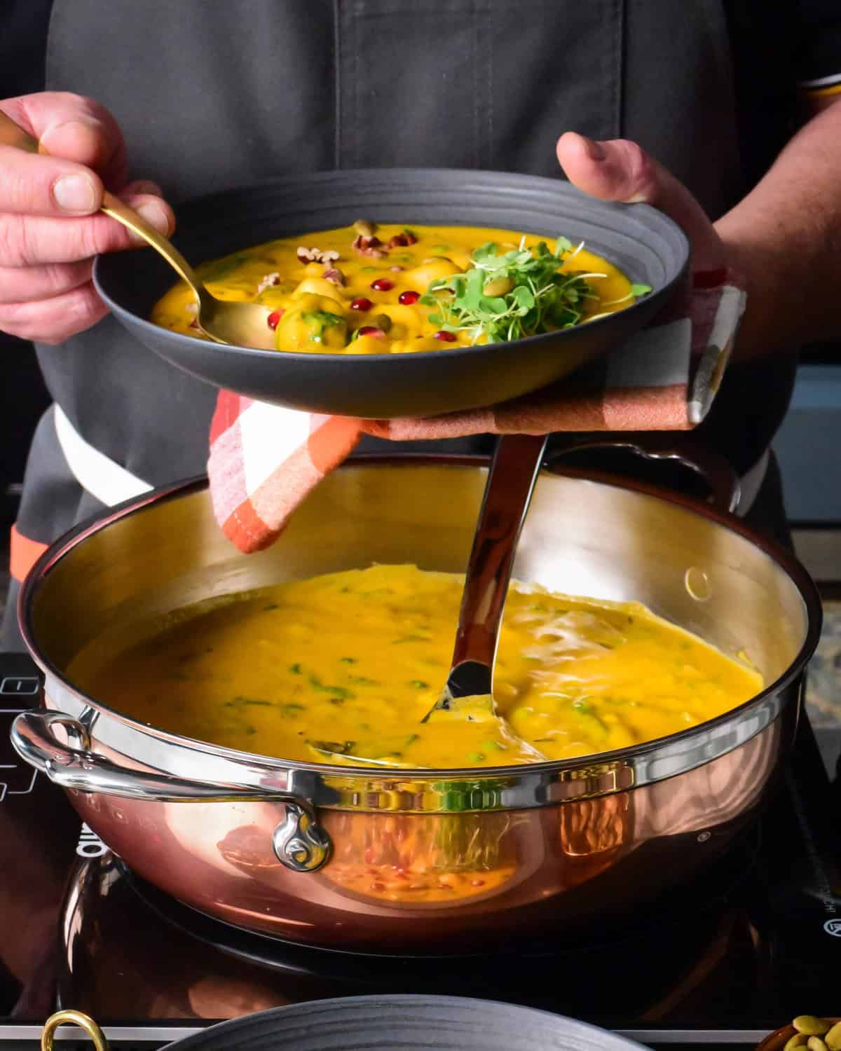 Holding a bowl of creamy sunshine squash soup with gnocchi, spinach and other toppings.