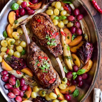 A pan of Diavola Veal Chops with Chili Apple Cider Glaze served with roasted grapes and peaches.