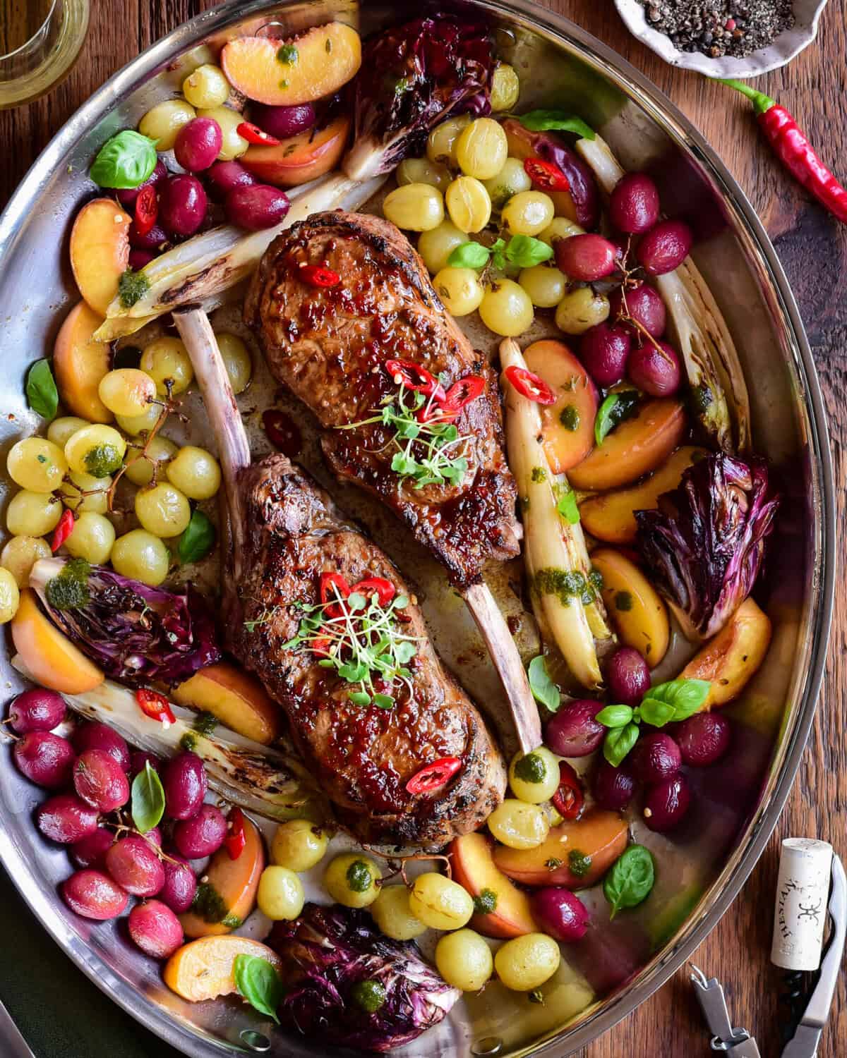 A pan of Diavola Veal Chops with Chili Apple Cider Glaze served with roasted grapes and peaches.