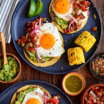 Two plates, each with two huevos rancheros tostadas and pieces of corn.