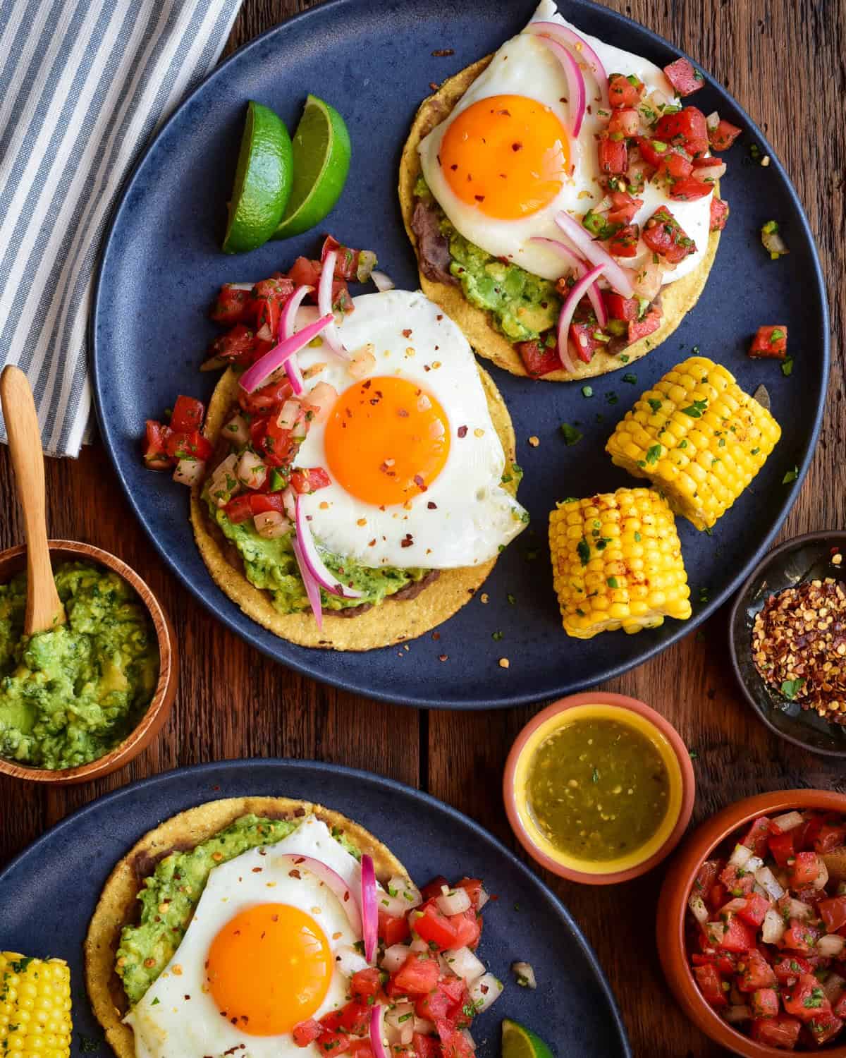 Two plates, each with two huevos rancheros tostadas and pieces of corn.