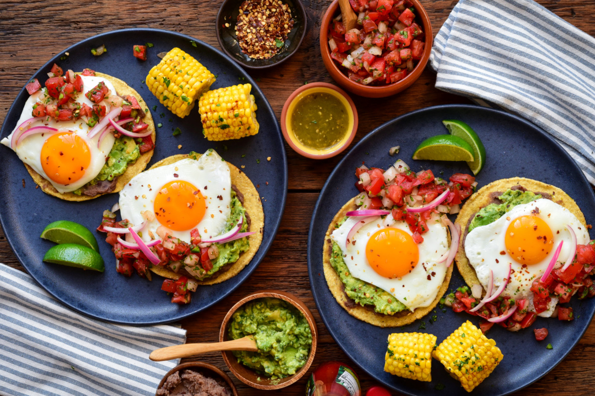 Two plates, each with two huevos rancheros tostadas and pieces of corn.